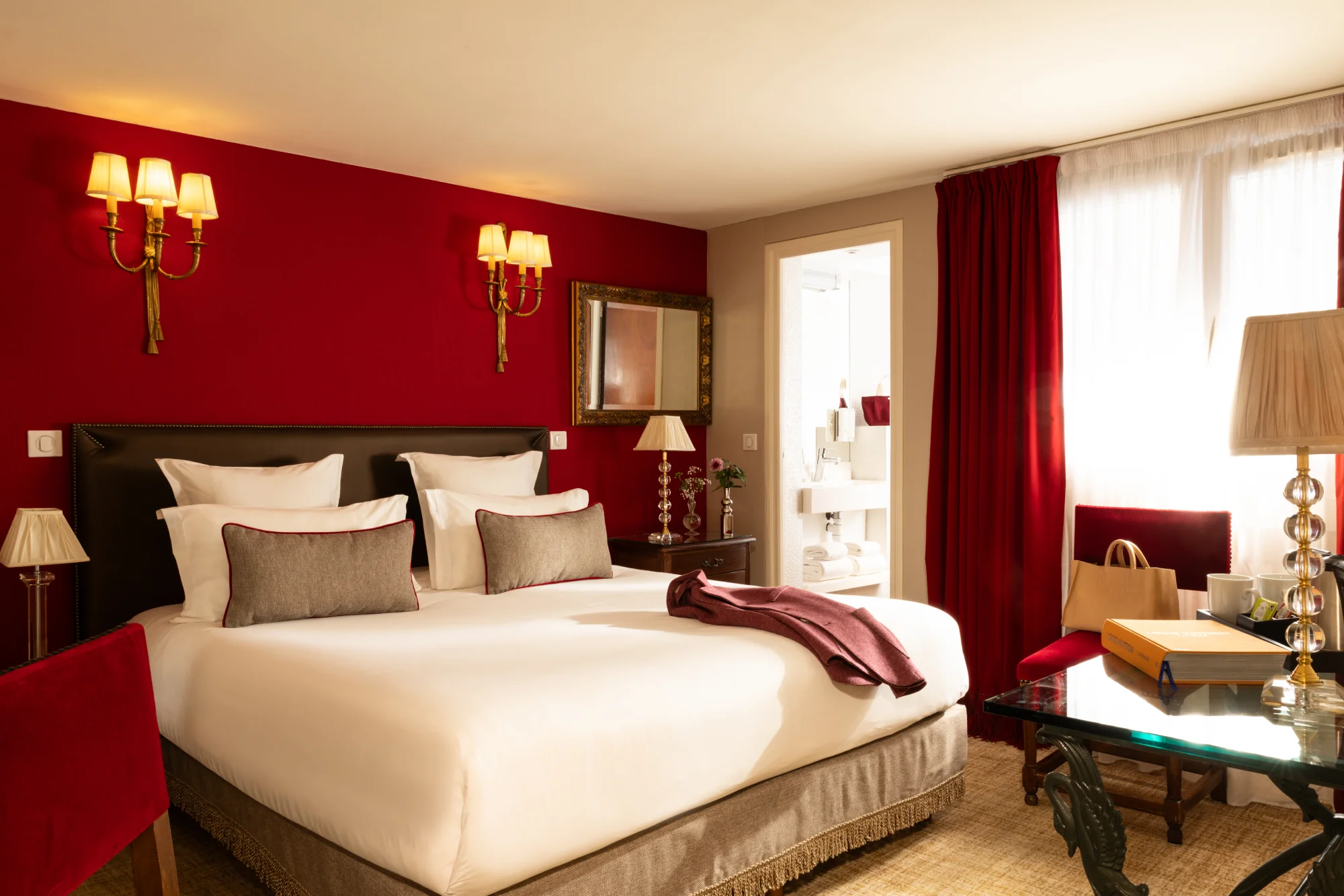 Miroir encadré doré au-dessus d'une table de chevet en bois avec lampe et roses, mur rouge de la chambre