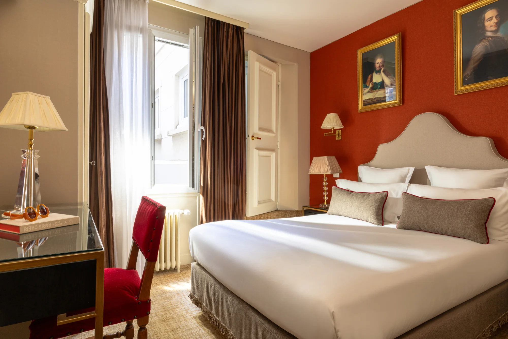 Vue d'ensemble d'une chambre au mur orangé avec portraits encadrés, lit et coin bureau, Hôtel des Deux Continents
