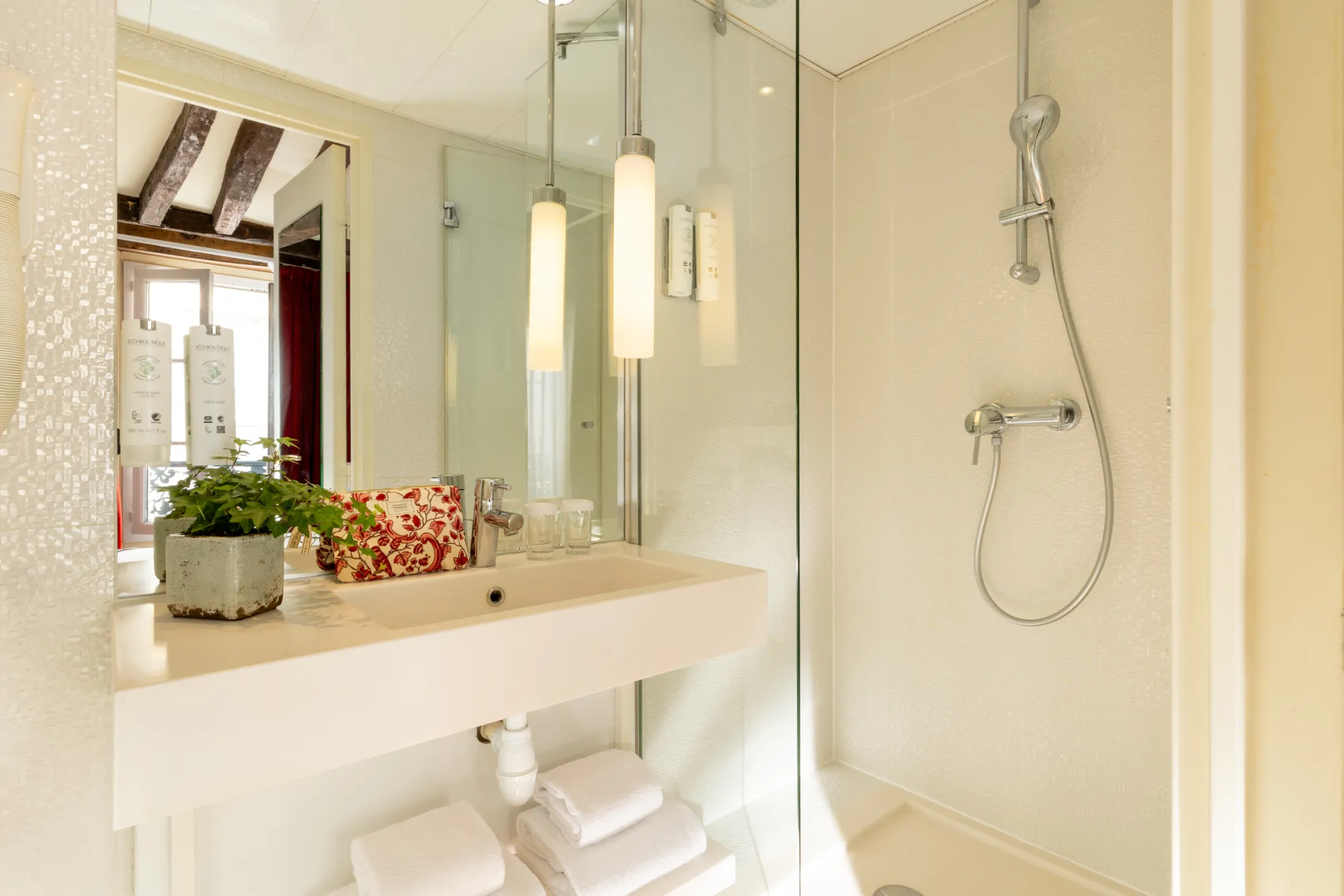 Vasque en marbre et suspensions lumineuses sous poutres apparentes dans la salle de bain de la chambre Classique de l'Hôtel des Deux Continents