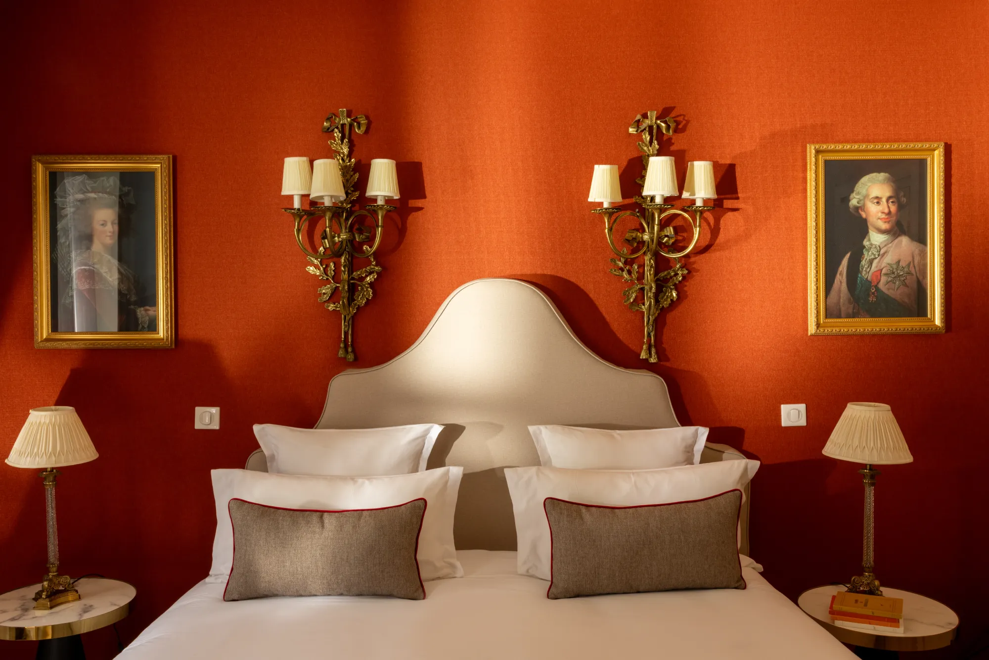 Lit avec tête de lit capitonnée encadré de deux portraits anciens et appliques en fer forgé dans la chambre Deluxe de l'Hôtel des Deux Continents