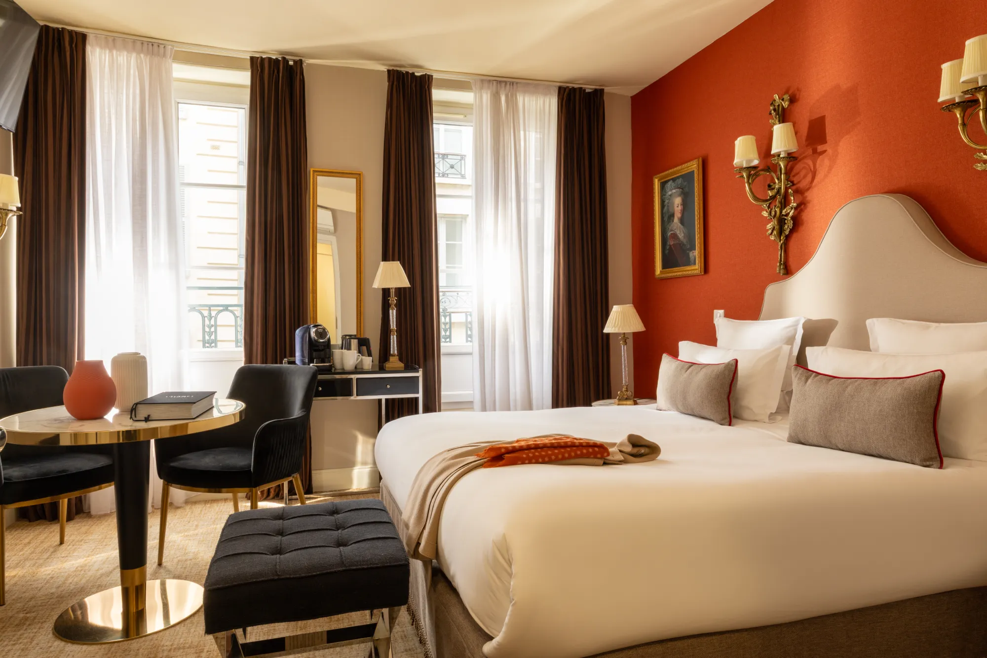 Grandes fenêtres offrant une vue panoramique sur les façades parisiennes depuis la chambre Deluxe au mur orangé