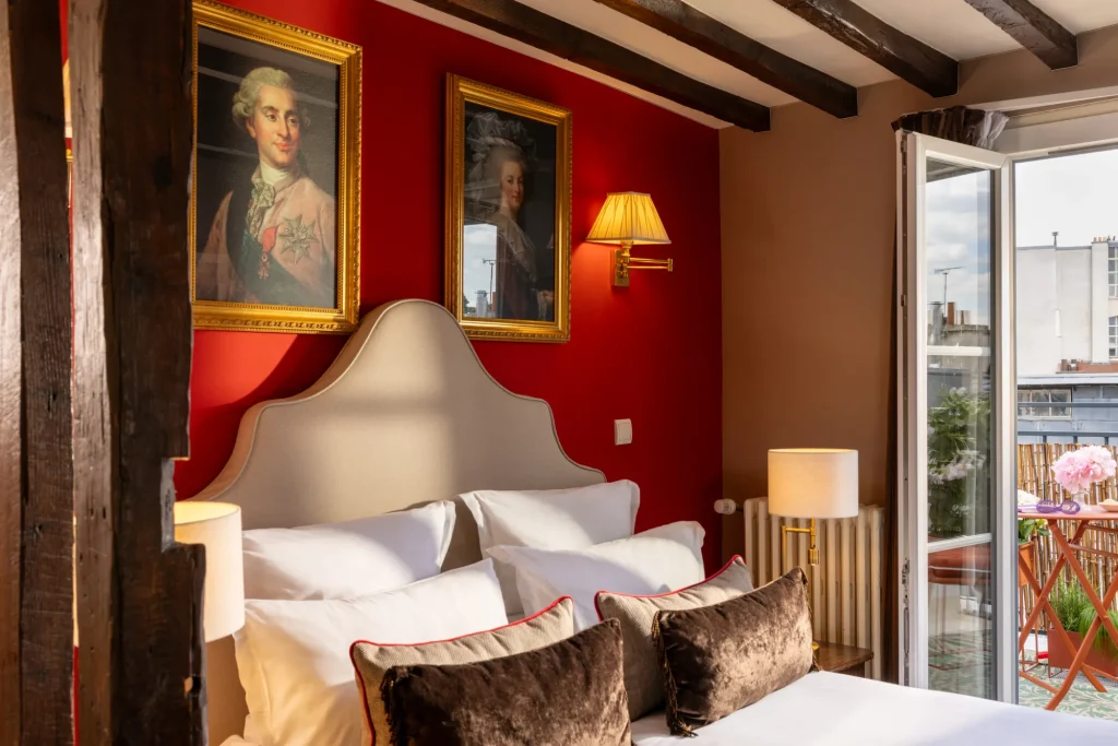 Chambre avec mur rouge, portraits encadrés et poutres apparentes à l'Hôtel des Deux Continents
