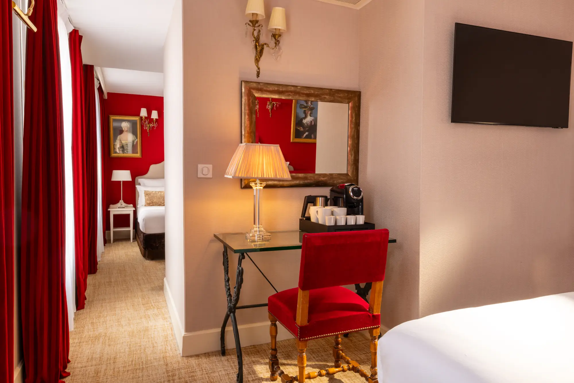 Bureau avec miroir, lampe et machine à café, avec vue sur la seconde chambre à travers une porte ouverte
