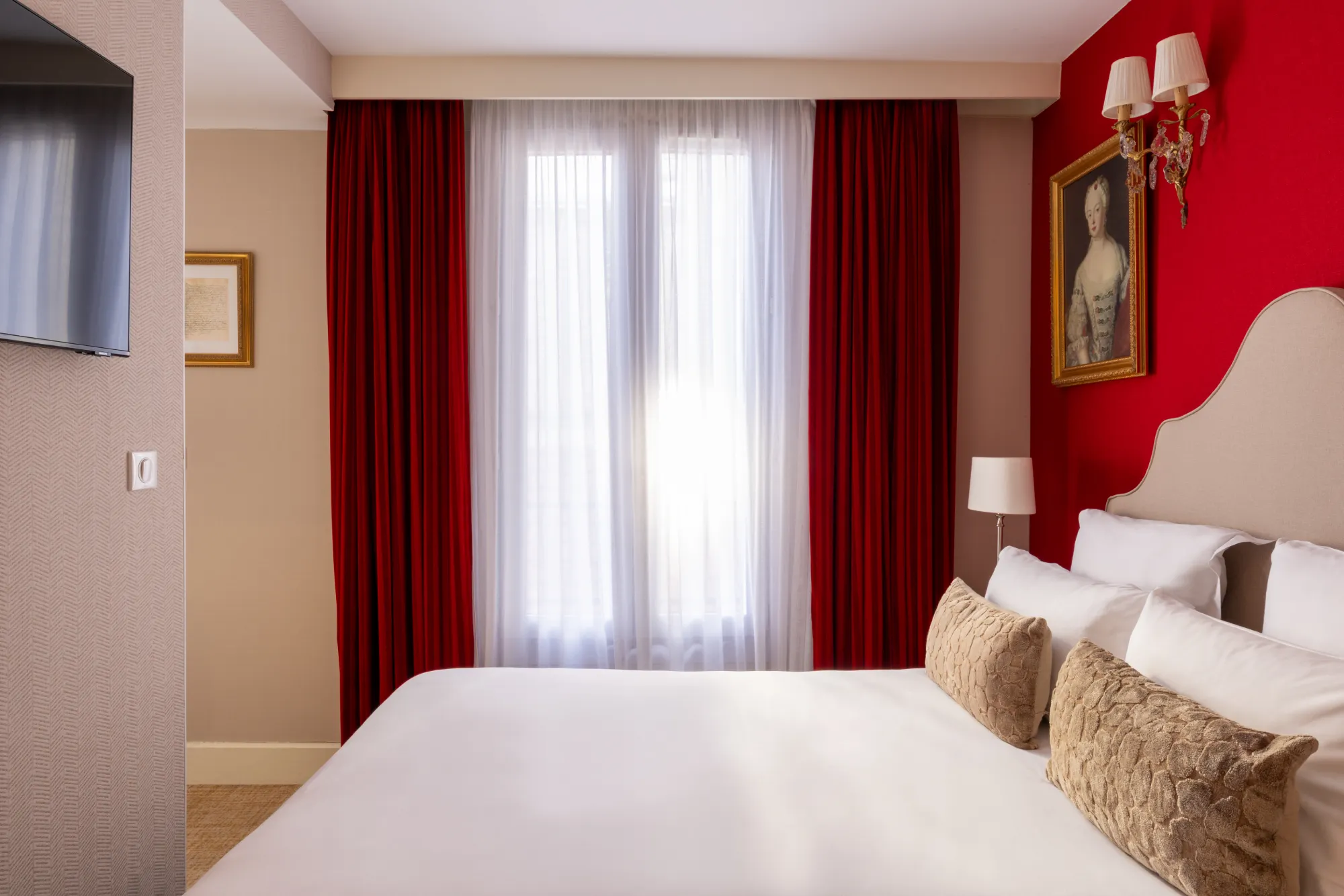 Lit avec rideaux rouges ouverts laissant entrer la lumière du jour dans la chambre familiale de l'Hôtel des Deux Continents