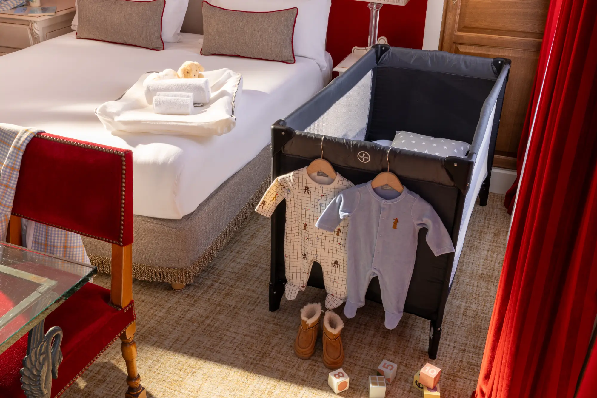 Lit parapluie pour bébé avec pyjamas suspendus et chaussons, au pied du lit dans la chambre familiale de l'Hôtel des Deux Continents