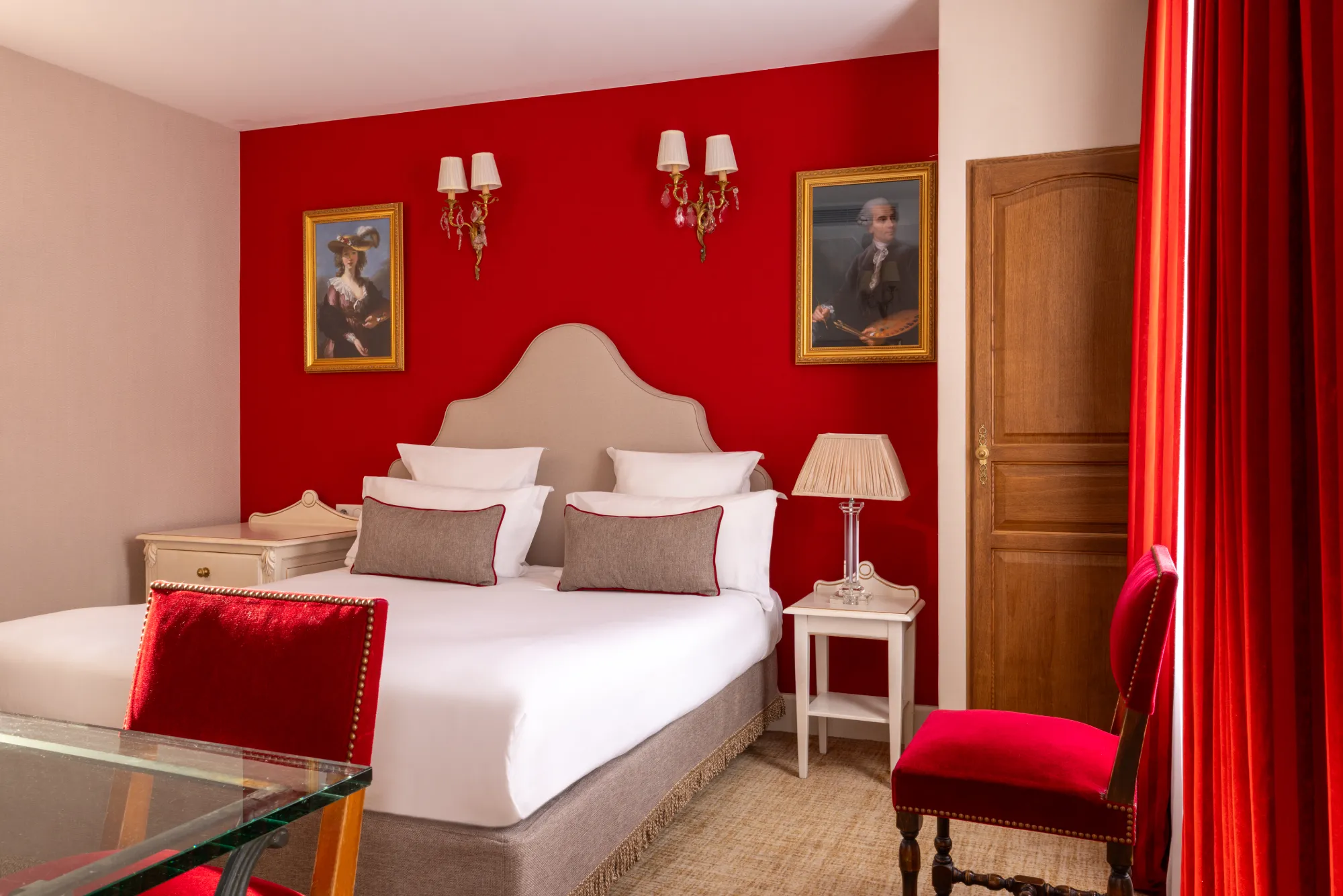 Chambre familiale avec mur rouge, portraits encadrés et appliques murales à l'Hôtel des Deux Continents