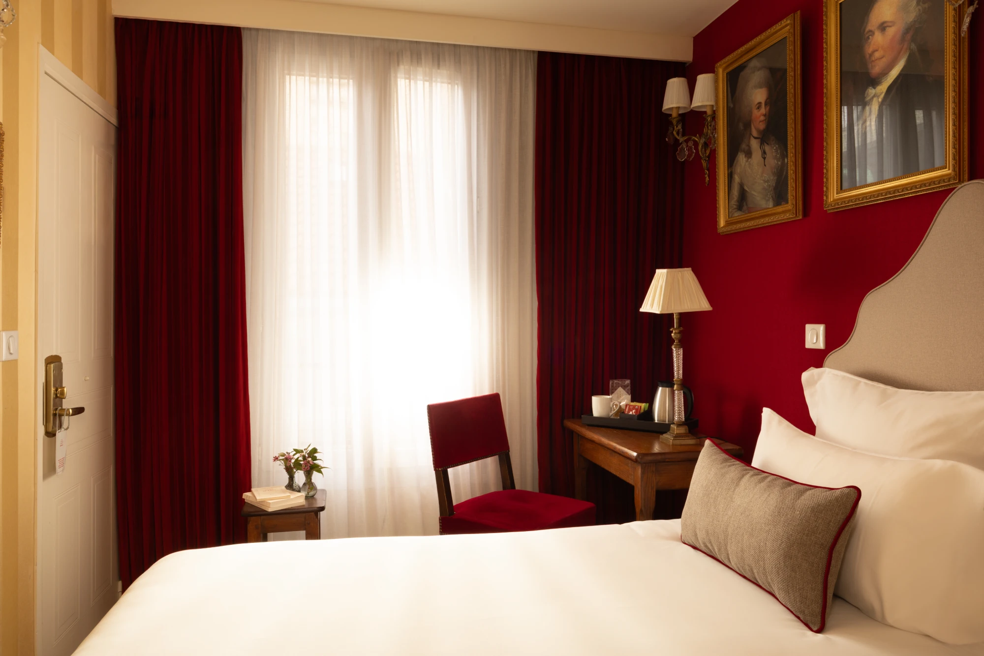 Chambre Single avec bureau en bois, chaise en velours rouge et rideaux assortis à l'Hôtel des Deux Continents