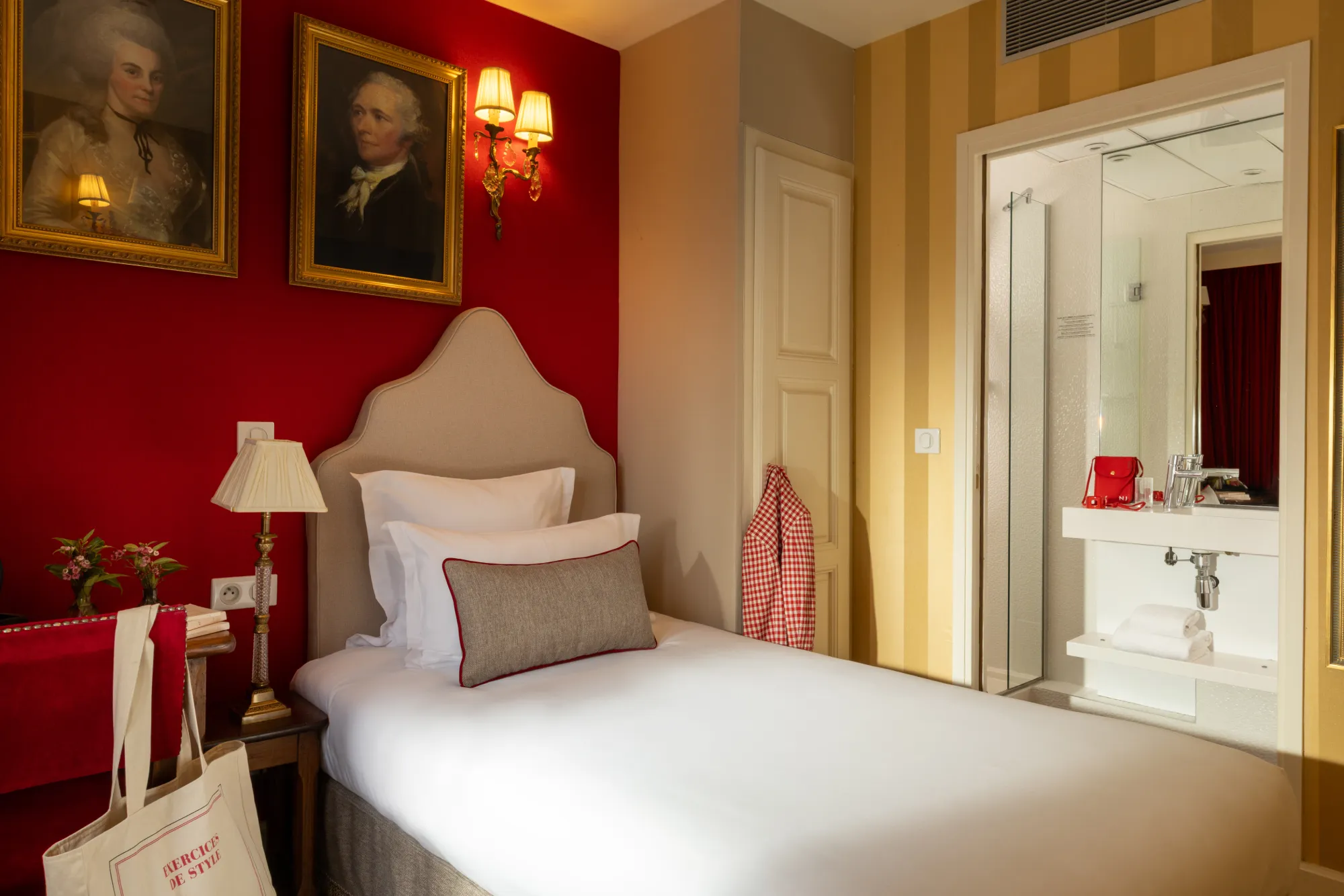 Chambre Single avec tête de lit rouge, portraits anciens et vue sur la salle d'eau attenante à l'Hôtel des Deux Continents