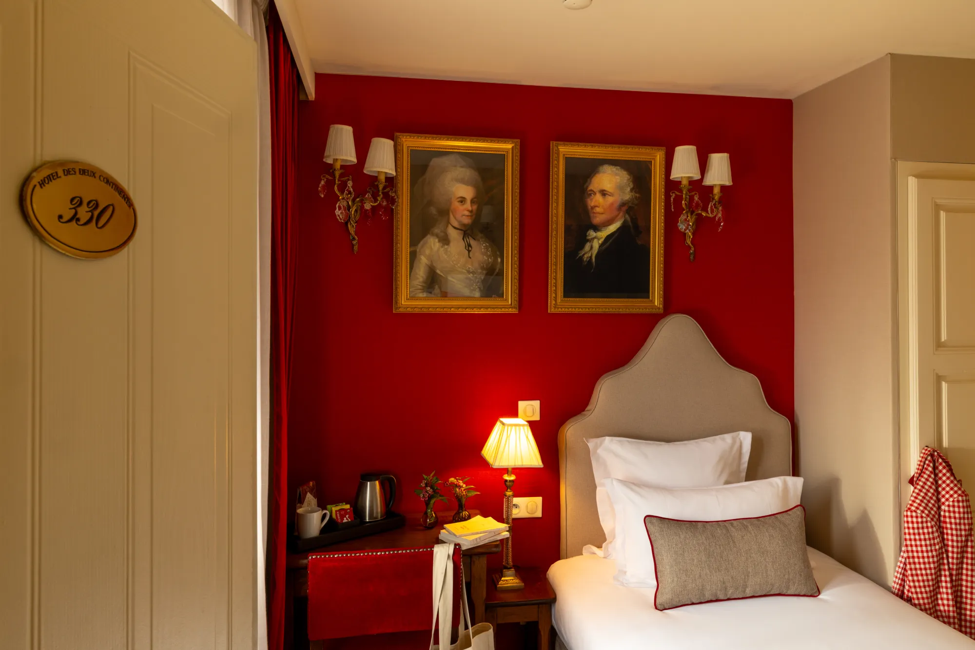 Porte d'entrée numérotée et mur orné de portraits anciens dans la chambre Single de l'Hôtel des Deux Continents