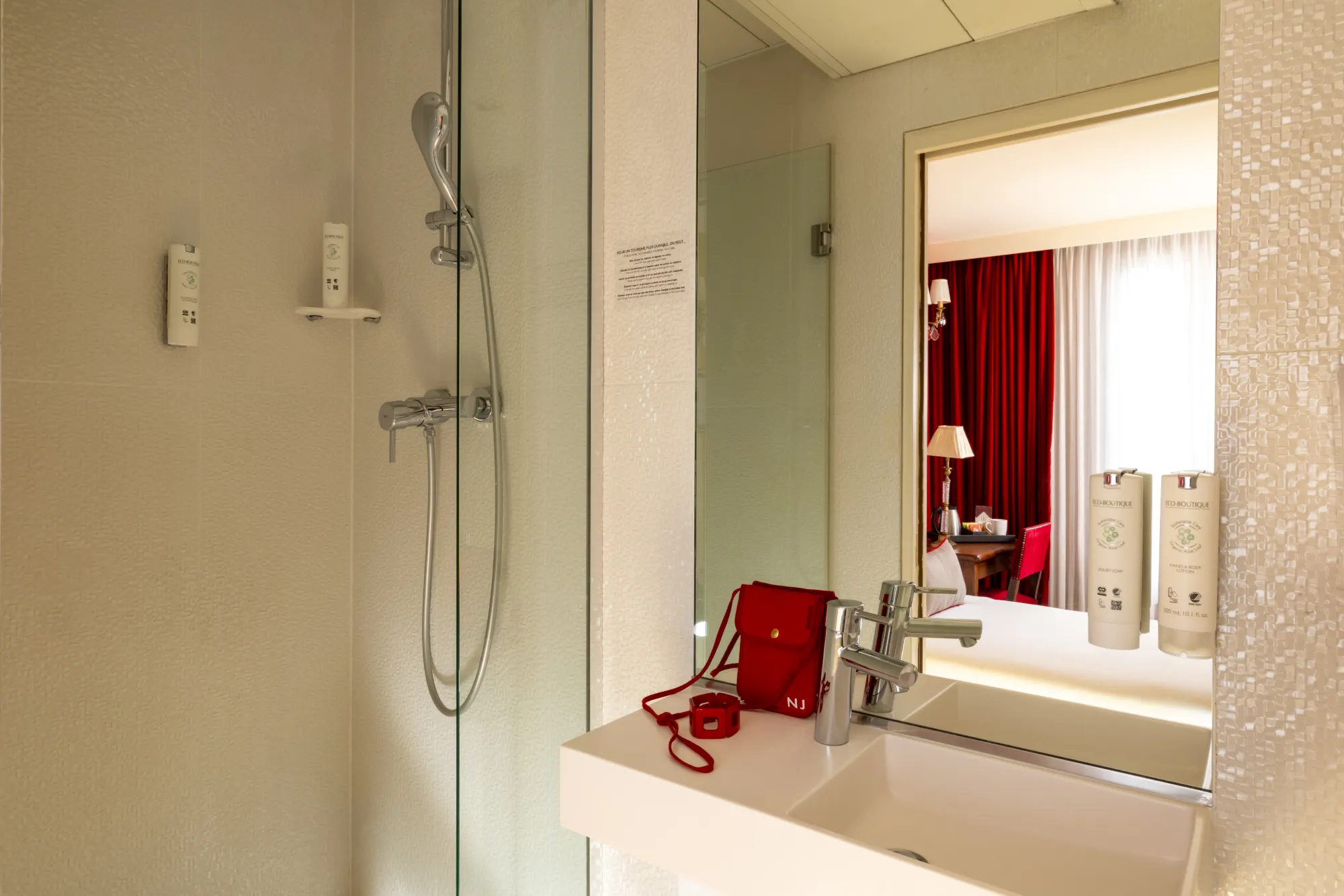 Douche vitrée et vasque en marbre reflétant les rideaux rouges de la chambre Single à l'Hôtel des Deux Continents