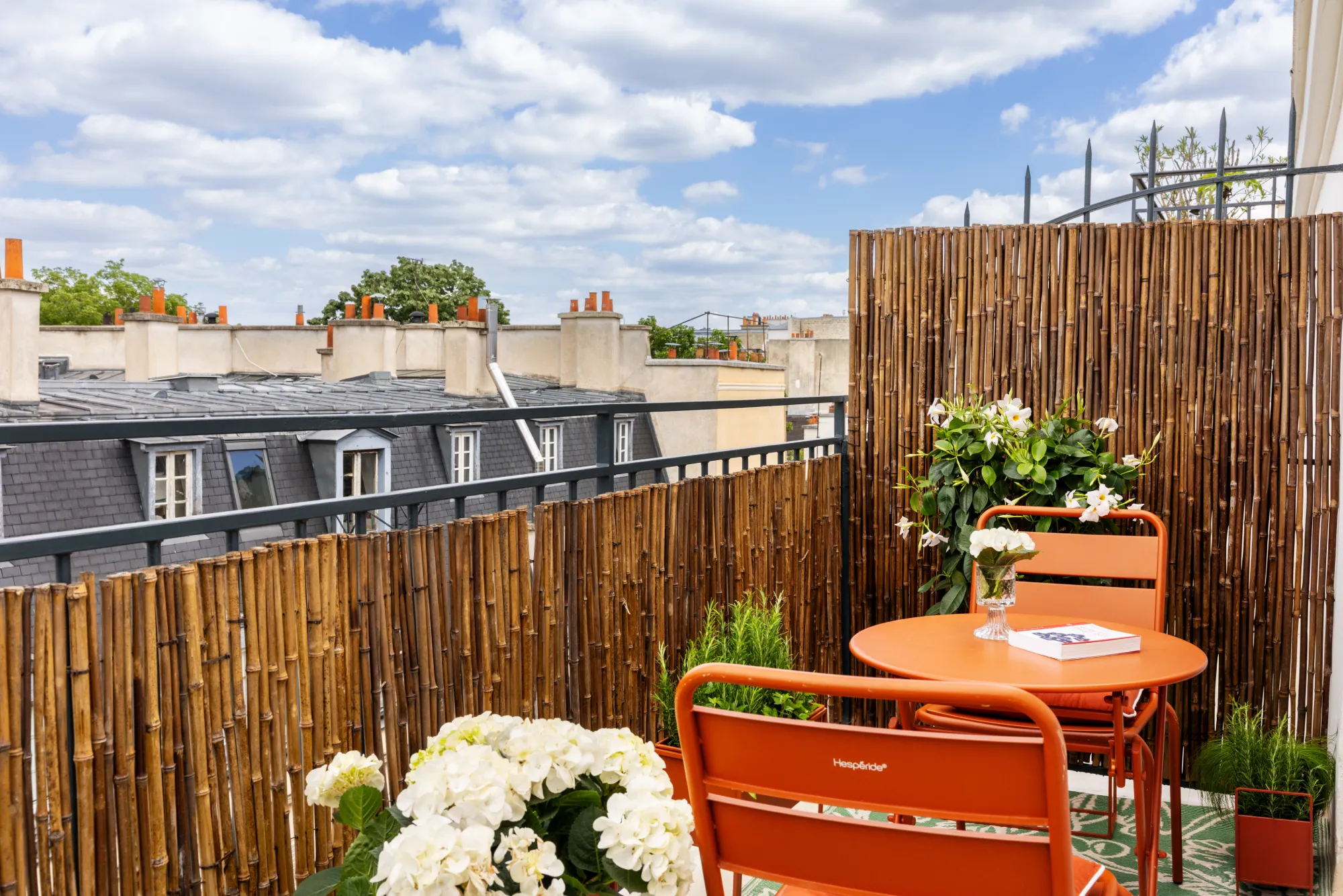 Terrasse avec mobilier orange, hortensias blancs et claustras en bambou surplombant les toits de Paris