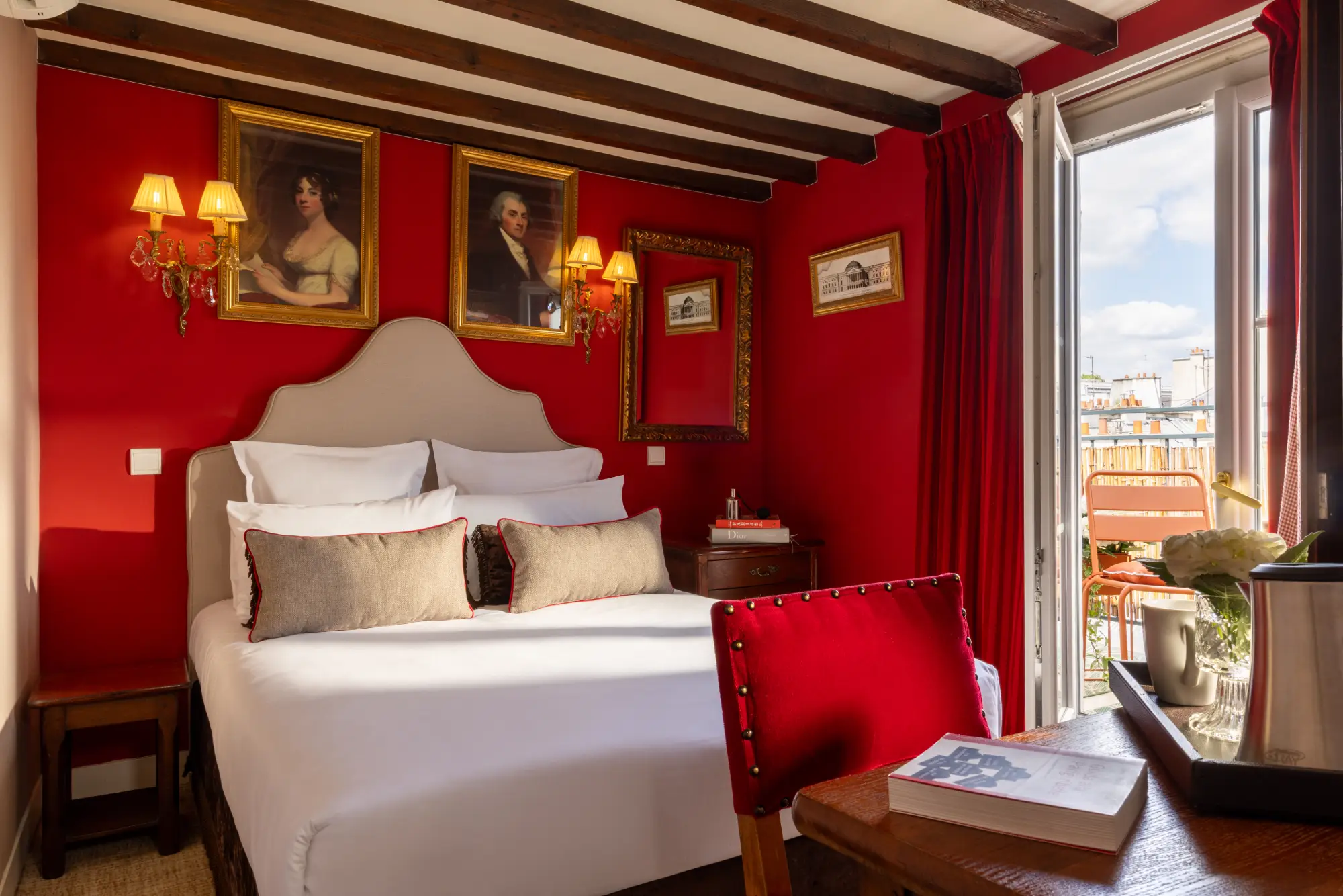 Chambre rouge avec poutres apparentes, portraits encadrés et porte-fenêtre ouverte sur la terrasse, Hôtel des Deux Continents