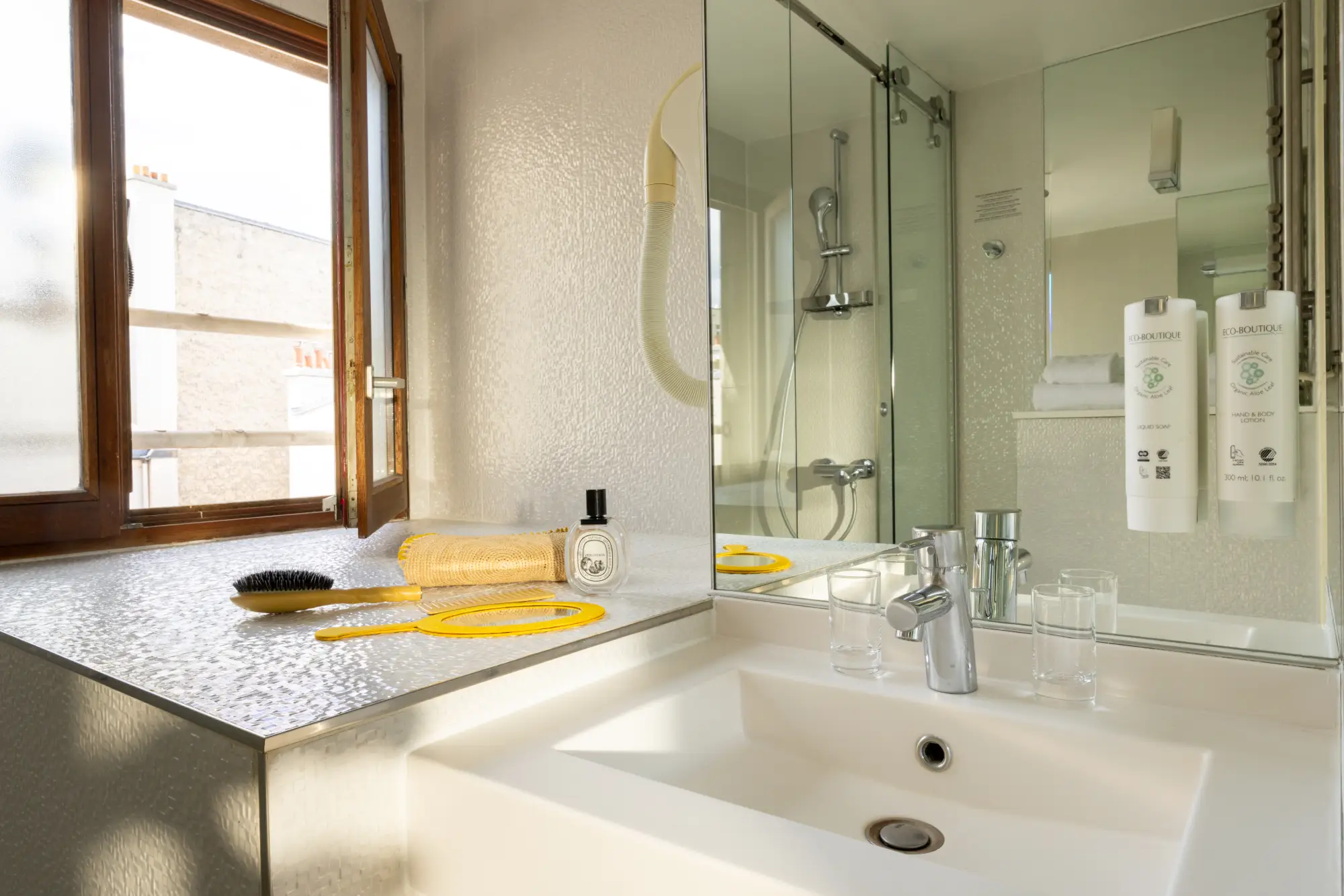 Vasque blanche sous une fenêtre, avec douche vitrée en reflet dans le miroir, Chambre Terrasse de l'Hôtel des Deux Continents