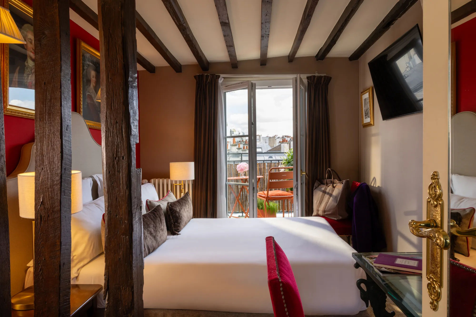Vue d'ensemble de la chambre avec poutres apparentes, linge de lit rouge et porte-fenêtre ouverte sur la terrasse, Hôtel des Deux Continents