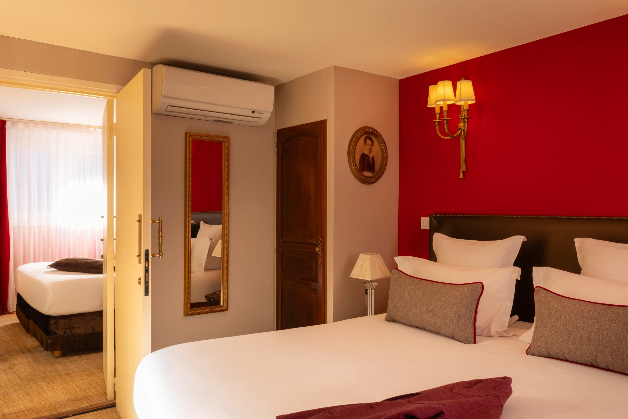 Lit avec tête de lit capitonnée et vue sur une seconde chambre par une porte ouverte dans les chambres communicantes
