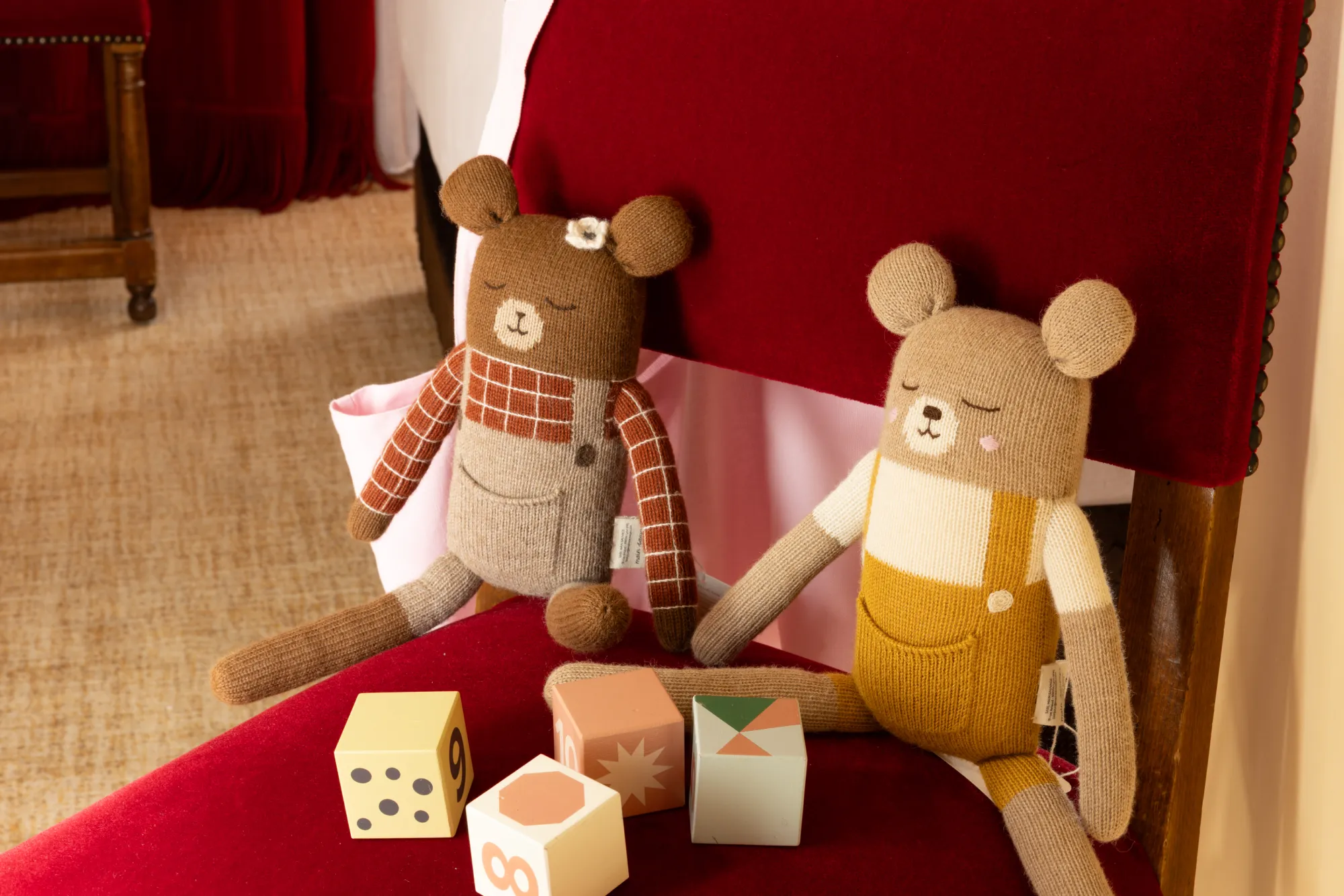 Peluches oursons et cubes en bois posés sur une banquette rouge dans la chambre communicante de l'Hôtel des Deux Continents