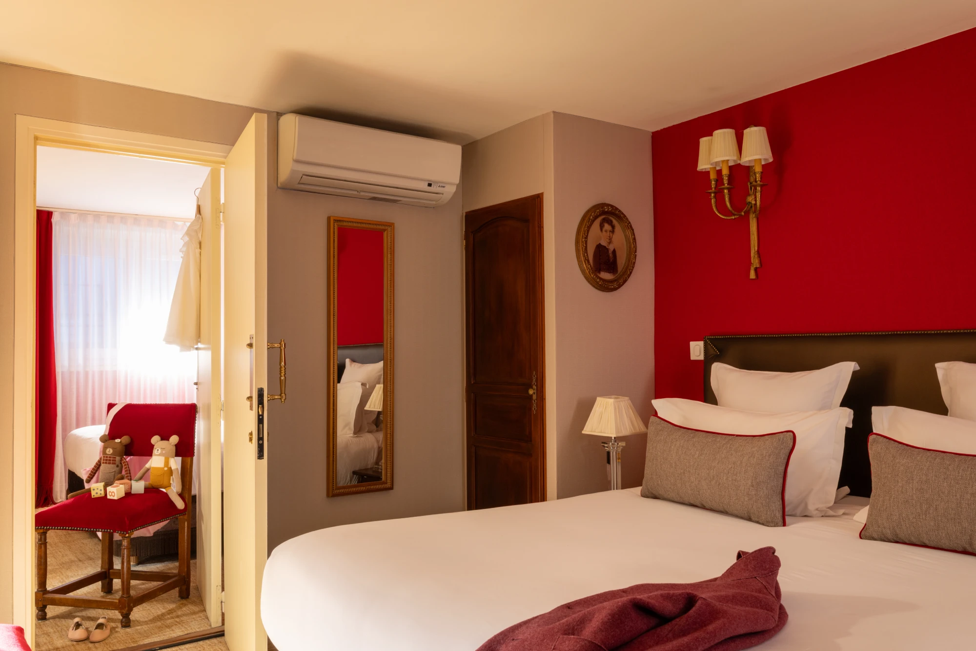 Chambre au mur rouge avec porte ouverte sur une seconde chambre communicante à l'Hôtel des Deux Continents