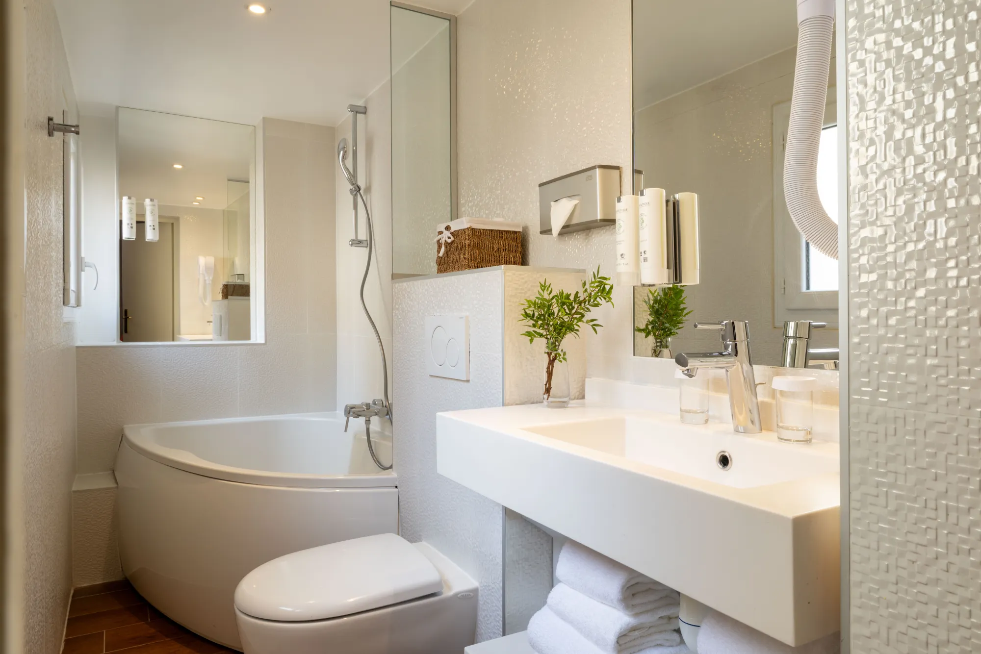 Salle de bain claire avec baignoire d'angle, douche vitrée et vasque en pierre blanche dans la Suite de l'Hôtel des Deux Continents