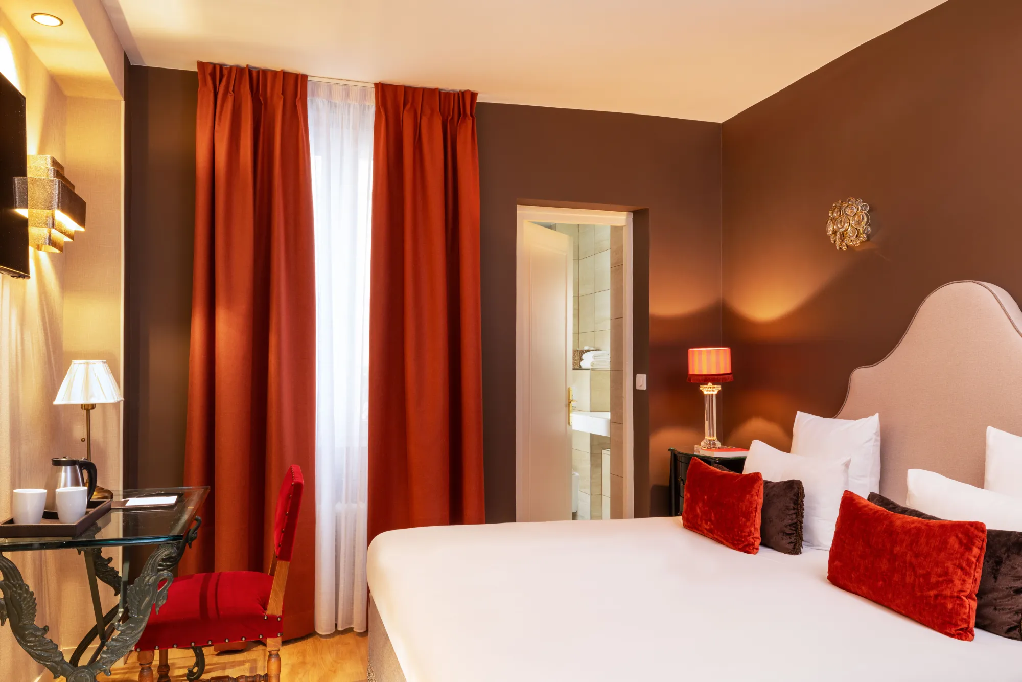 Suite spacieuse aux tons chocolat et rouge avec lit double et coin bureau à l'Hôtel des Deux Continents