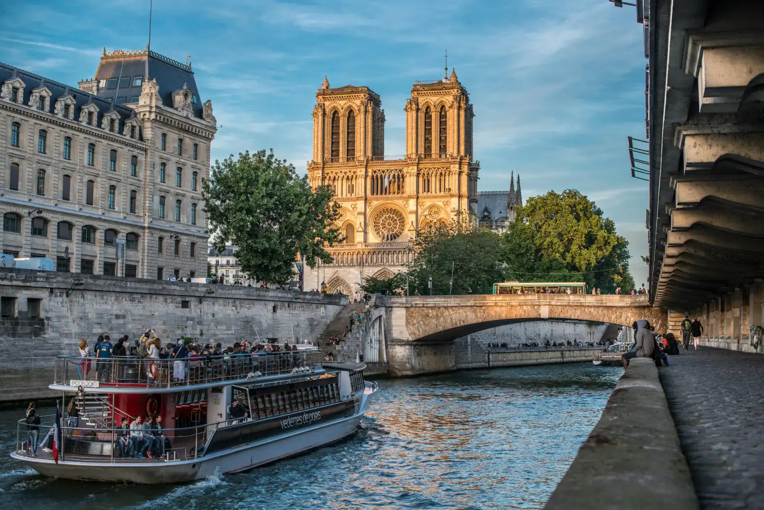 Cathédrale Notre-Dame de Paris et bateau-mouche naviguant sur la Seine au coucher du soleil