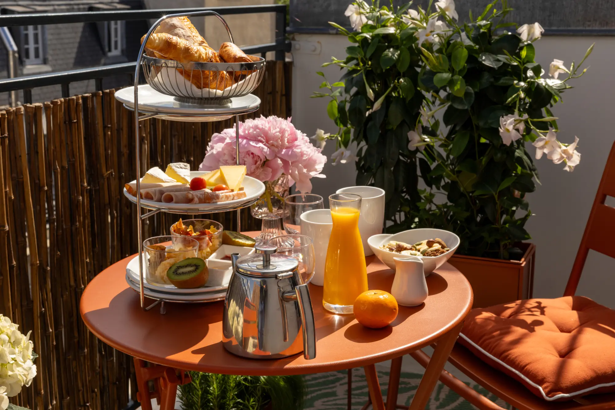 Table de petit-déjeuner dressée sur une terrasse fleurie avec vue sur les toits de Paris