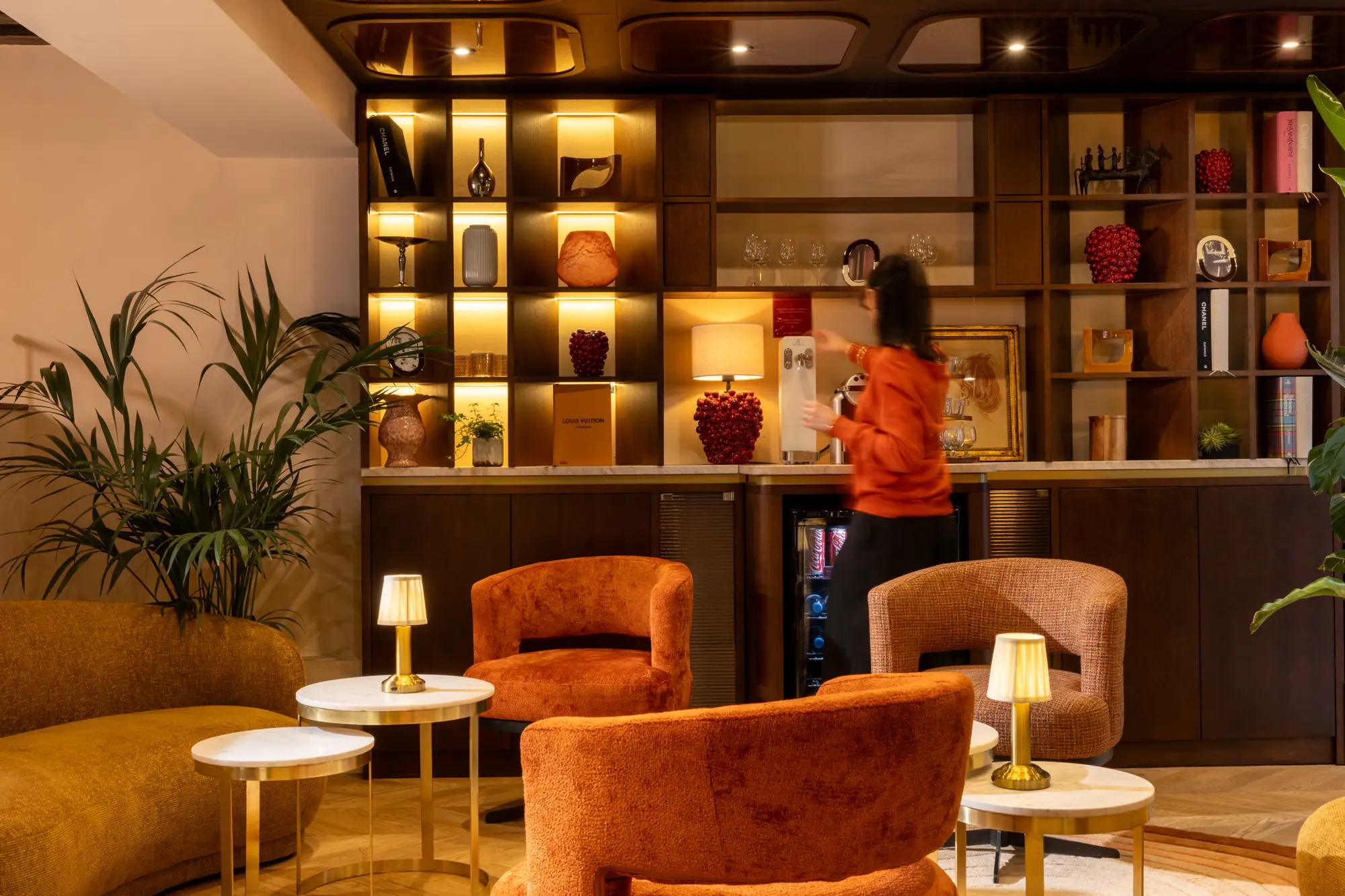 Espace bar-lounge avec étagère décorative et fauteuils orangés à l'Hôtel des Deux Continents